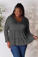 Woman wearing a plus size dark gray long sleeve ruffle top with buttons and blue jeans