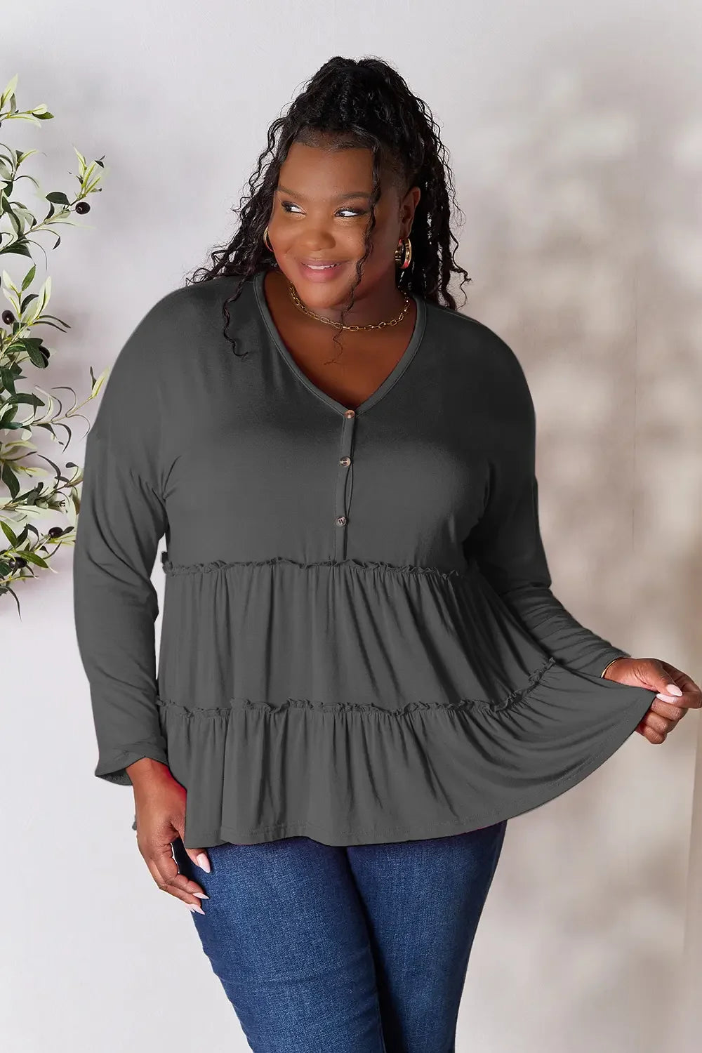 Woman wearing a plus size dark gray long sleeve ruffle top with buttons and blue jeans