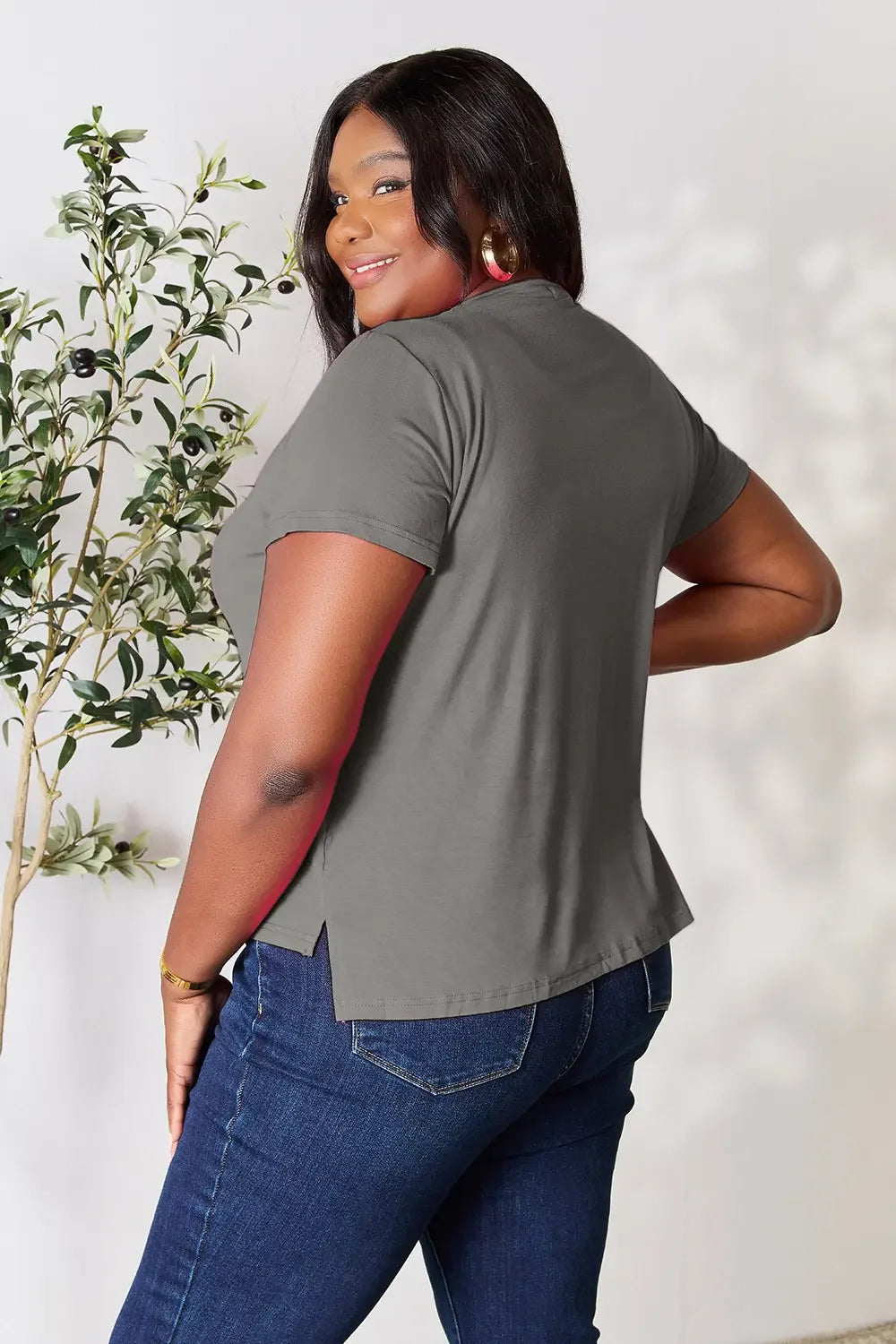 Woman modeling casual grey short sleeve top and blue jeans, smiling indoors