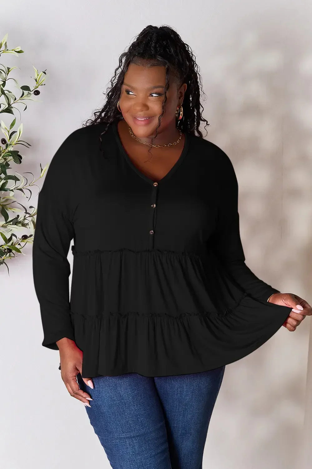 Woman wearing a black long sleeve ruffled top with buttons and blue jeans.