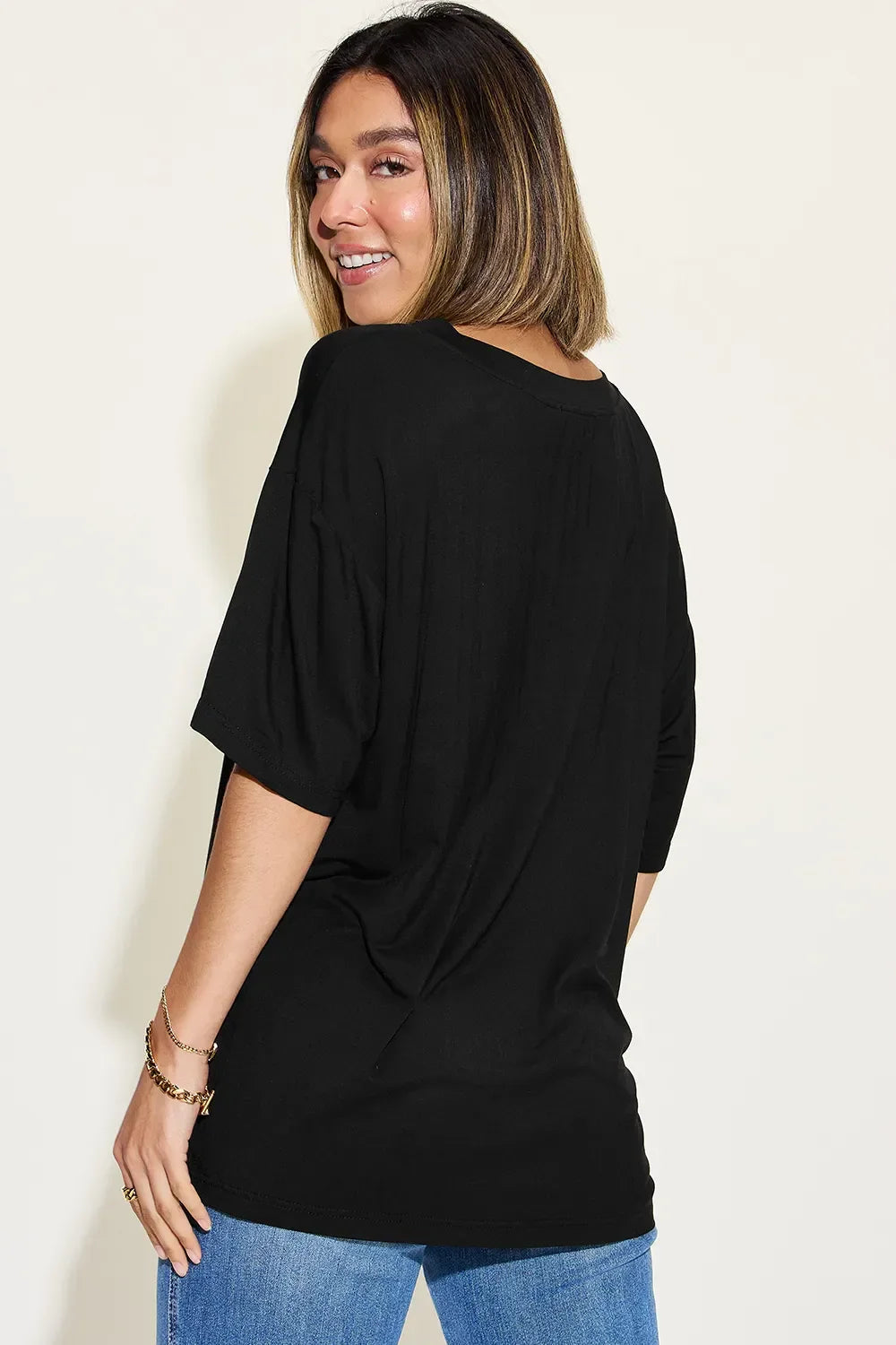 Woman wearing a loose black short sleeve top and blue jeans, shown from the back.