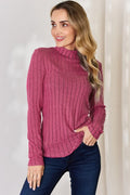 Woman wearing a pink ribbed long sleeve turtleneck top and dark jeans