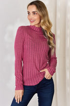 Woman wearing a pink ribbed long sleeve turtleneck top and dark jeans