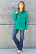 Woman in green long sleeve top and blue jeans, casual fashion, standing by concrete wall