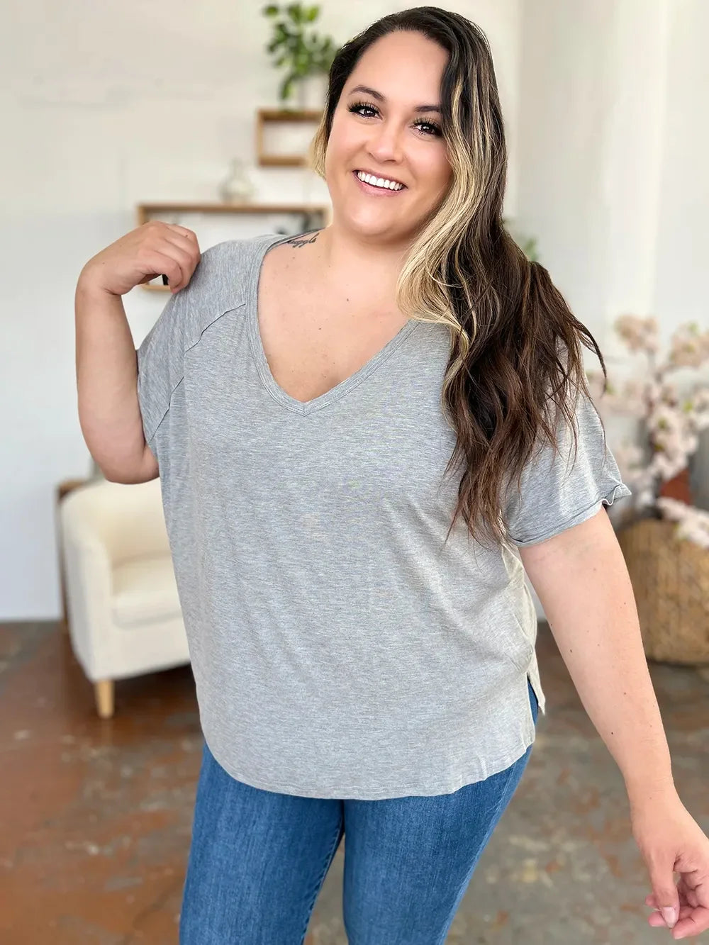 Woman in a casual grey v-neck t-shirt and blue jeans smiling indoors