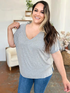 Woman in a casual grey v-neck t-shirt and blue jeans smiling indoors