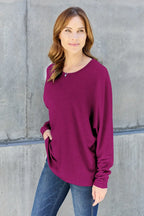 Woman wearing a long sleeve purple top and blue jeans standing against a concrete wall