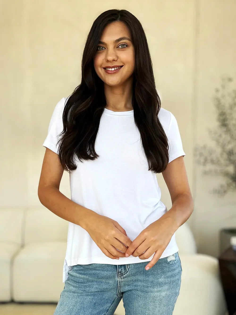 Woman in casual white t-shirt and blue jeans smiling indoors