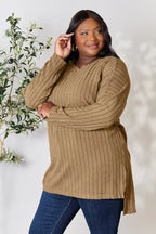 Woman wearing a ribbed tan knit sweater with long sleeves and blue jeans, standing indoors.