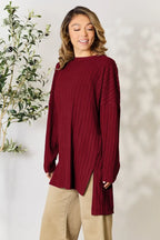 Woman wearing a long sleeve ribbed burgundy sweater with beige pants, standing indoors.