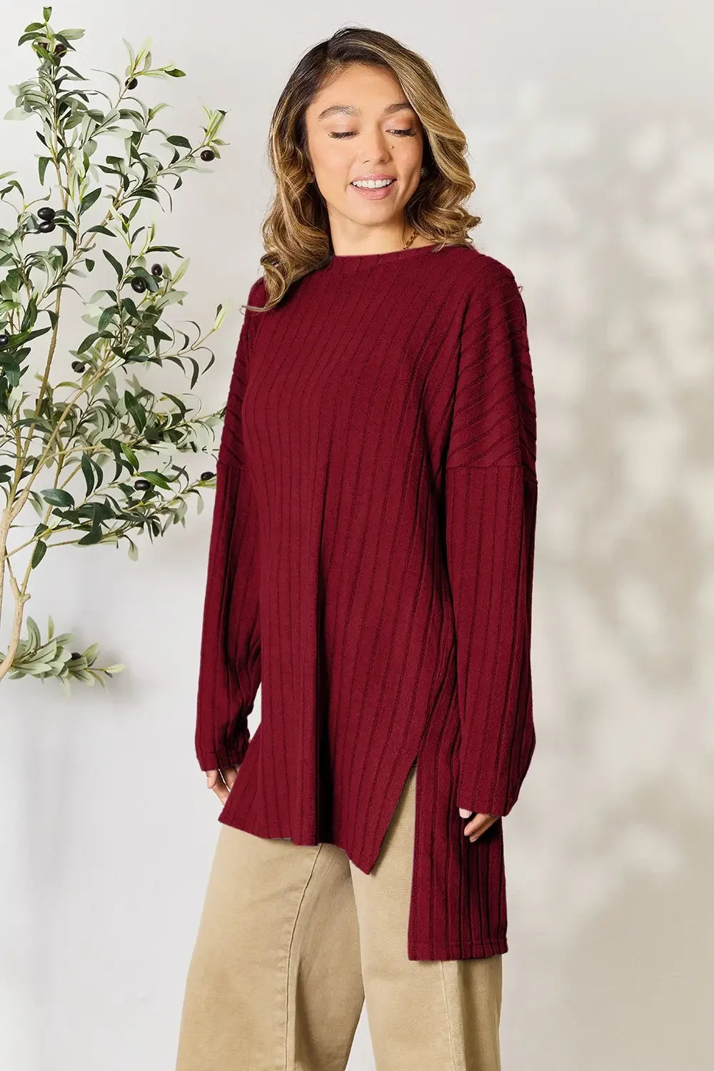 Woman wearing a long sleeve ribbed burgundy sweater with beige pants, standing indoors.