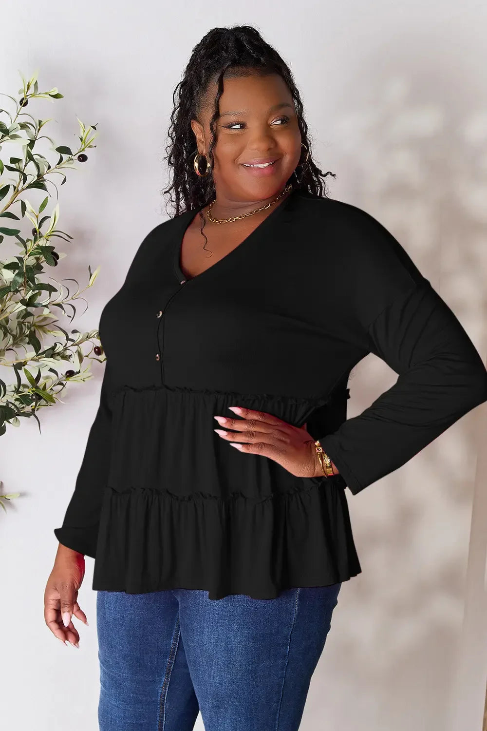 Smiling woman in a black long-sleeve tiered blouse and blue jeans, plus size fashion