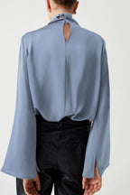 Back view of woman in light blue long sleeve blouse with keyhole detail and black pants