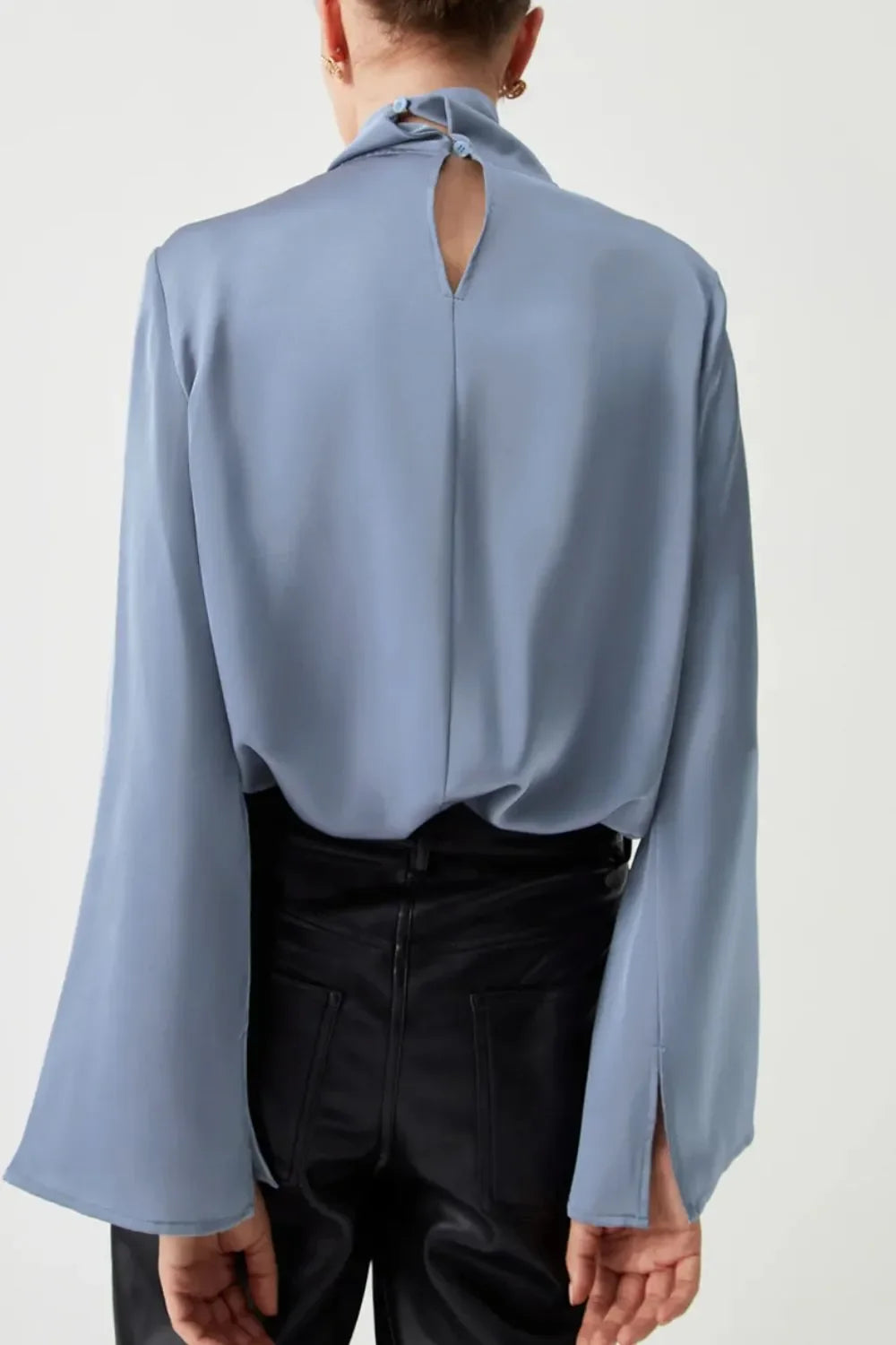 Back view of woman in light blue long sleeve blouse with keyhole detail and black pants