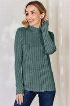 Woman in green ribbed knit long sleeve top and blue jeans standing indoors