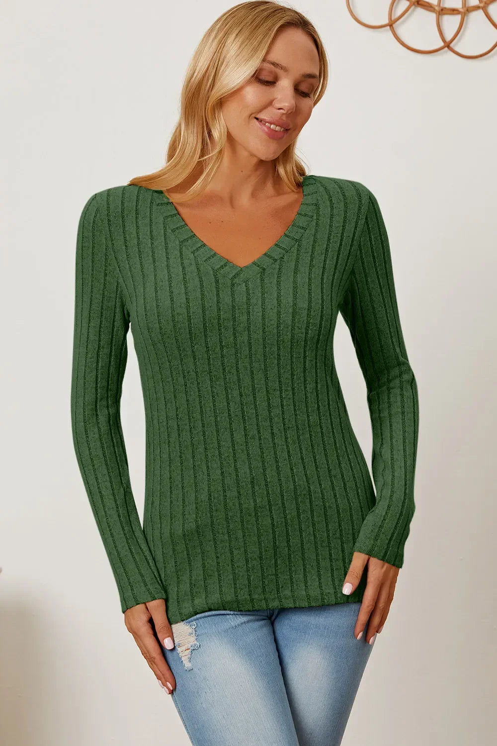 Woman wearing green ribbed knit V-neck sweater and light blue jeans