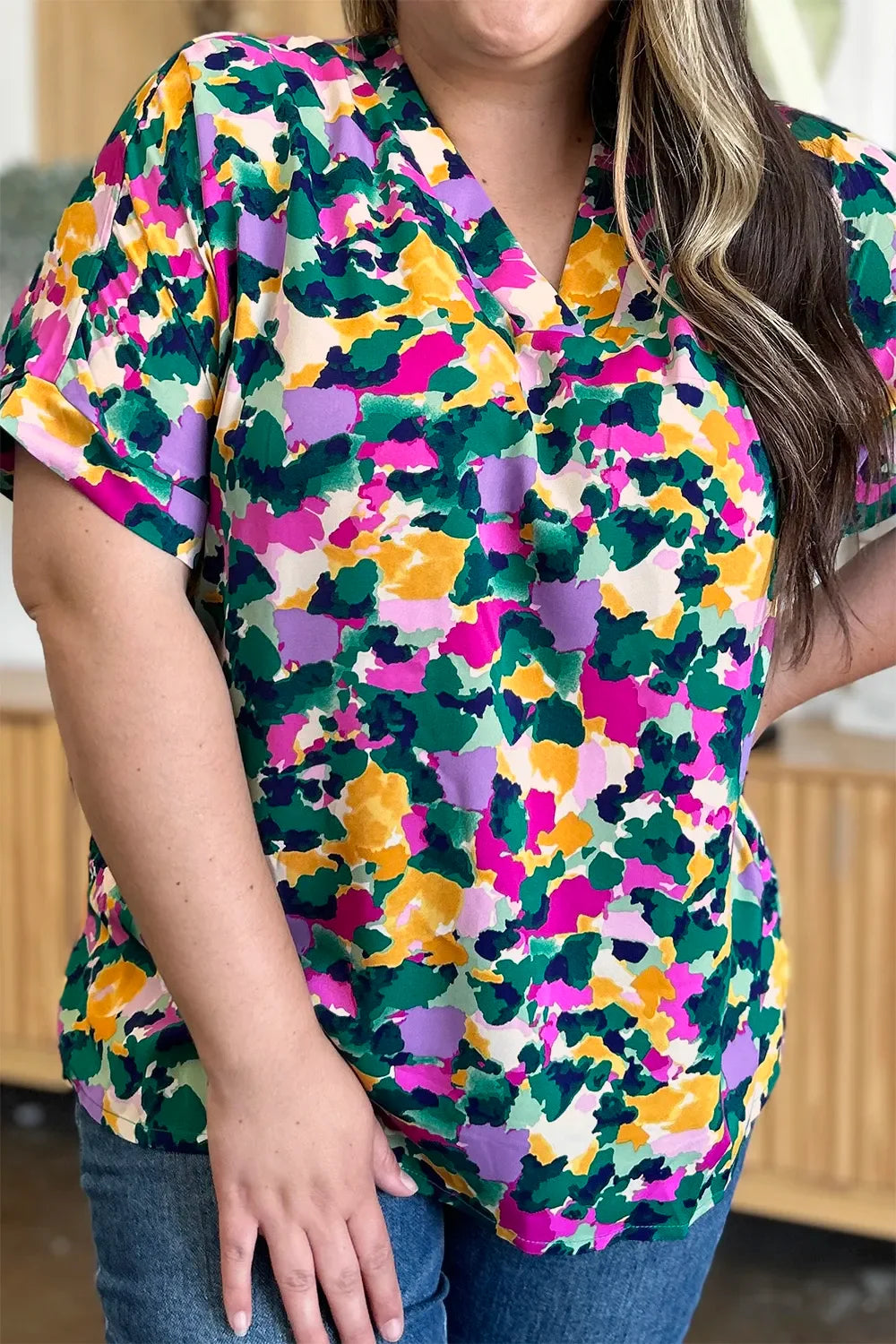 Woman wearing a colorful floral print short sleeve top with v-neck, paired with jeans