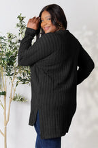 Woman wearing a black ribbed long-sleeve sweater tunic with side slits and blue jeans