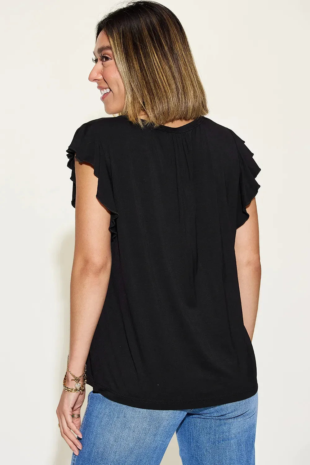 Woman wearing black ruffle sleeve top and blue jeans, shown from the back.