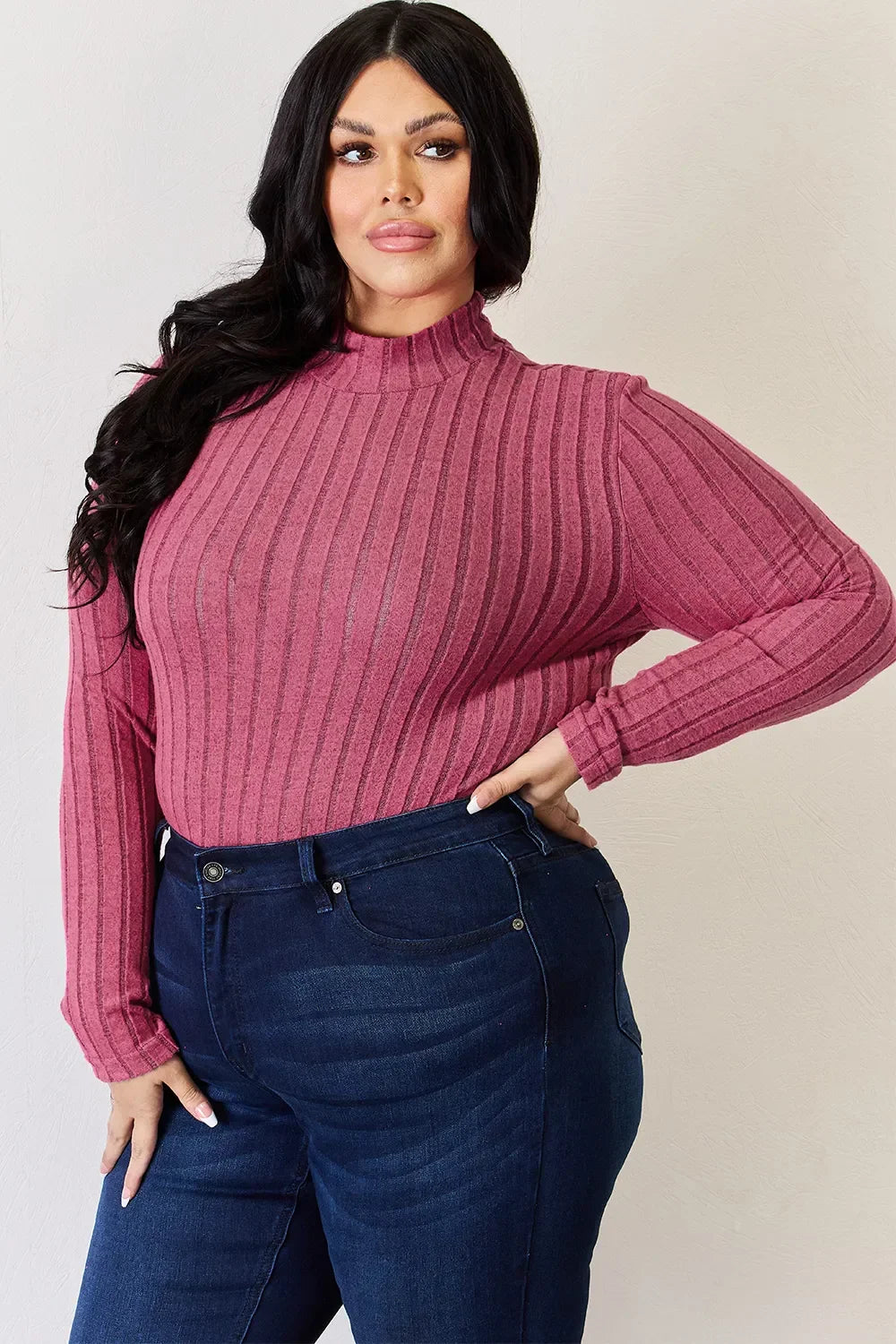 Woman wearing a ribbed pink long sleeve top and dark blue high-waisted jeans