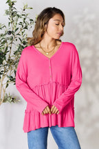 Woman wearing a bright pink long sleeve tiered blouse with buttons and blue jeans