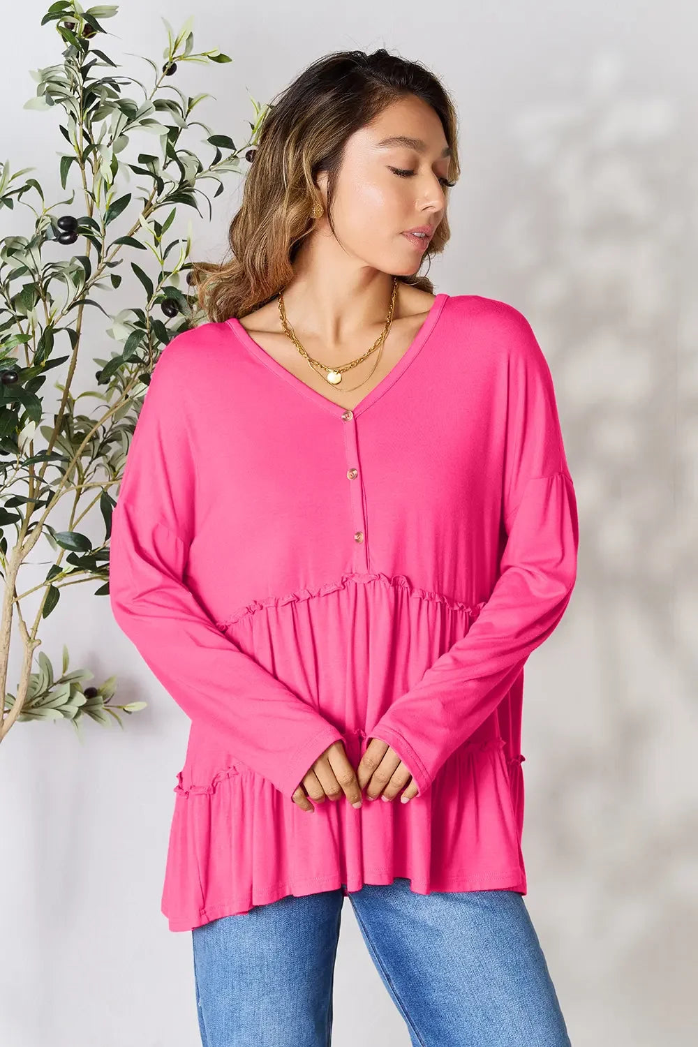 Woman wearing a bright pink long sleeve tiered blouse with buttons and blue jeans