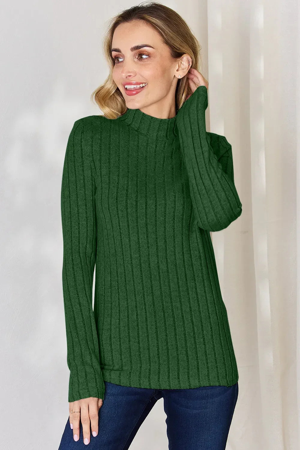 Woman wearing a green ribbed knit long sleeve sweater with mock neck and blue jeans