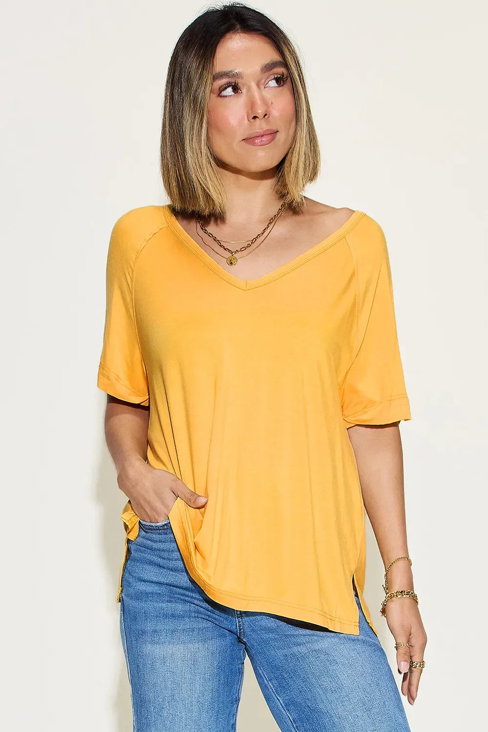 Woman wearing a casual yellow V-neck short sleeve top and blue jeans on neutral background