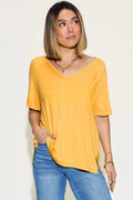 Woman wearing a casual yellow V-neck short sleeve top and blue jeans on neutral background