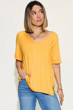 Woman wearing a casual yellow V-neck short sleeve top and blue jeans on neutral background