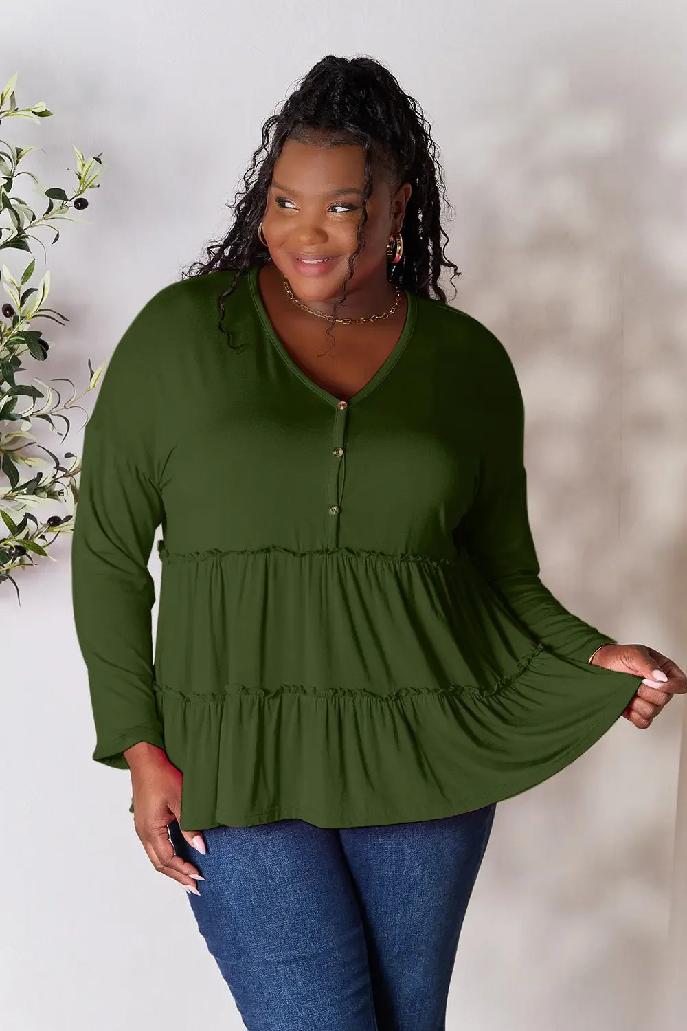 Plus size woman in long sleeve olive green tiered blouse and blue jeans