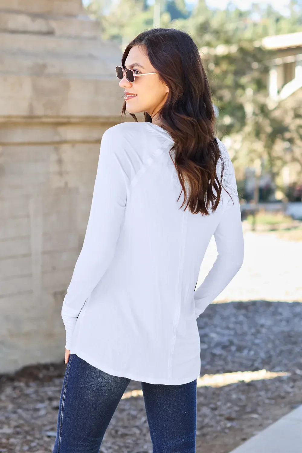 Woman in casual white long sleeve top and jeans outdoors, wearing sunglasses