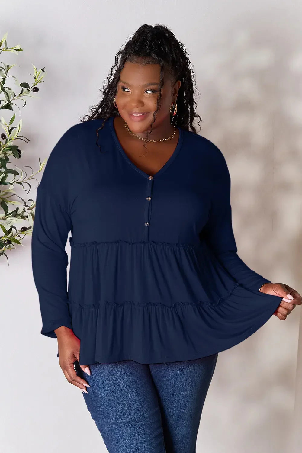 Plus size woman wearing a navy blue long sleeve tiered blouse and blue jeans
