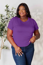 Woman in a purple short sleeve t-shirt and blue jeans posing in front of a plant
