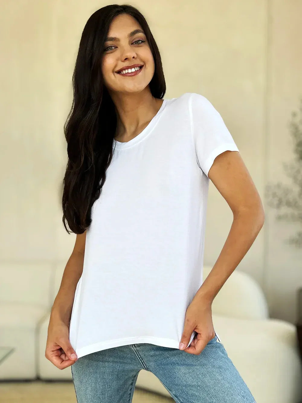 Woman wearing plain white short sleeve t-shirt and blue jeans, standing indoors