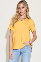 Woman in yellow short sleeve V-neck t-shirt and light blue jeans on neutral background