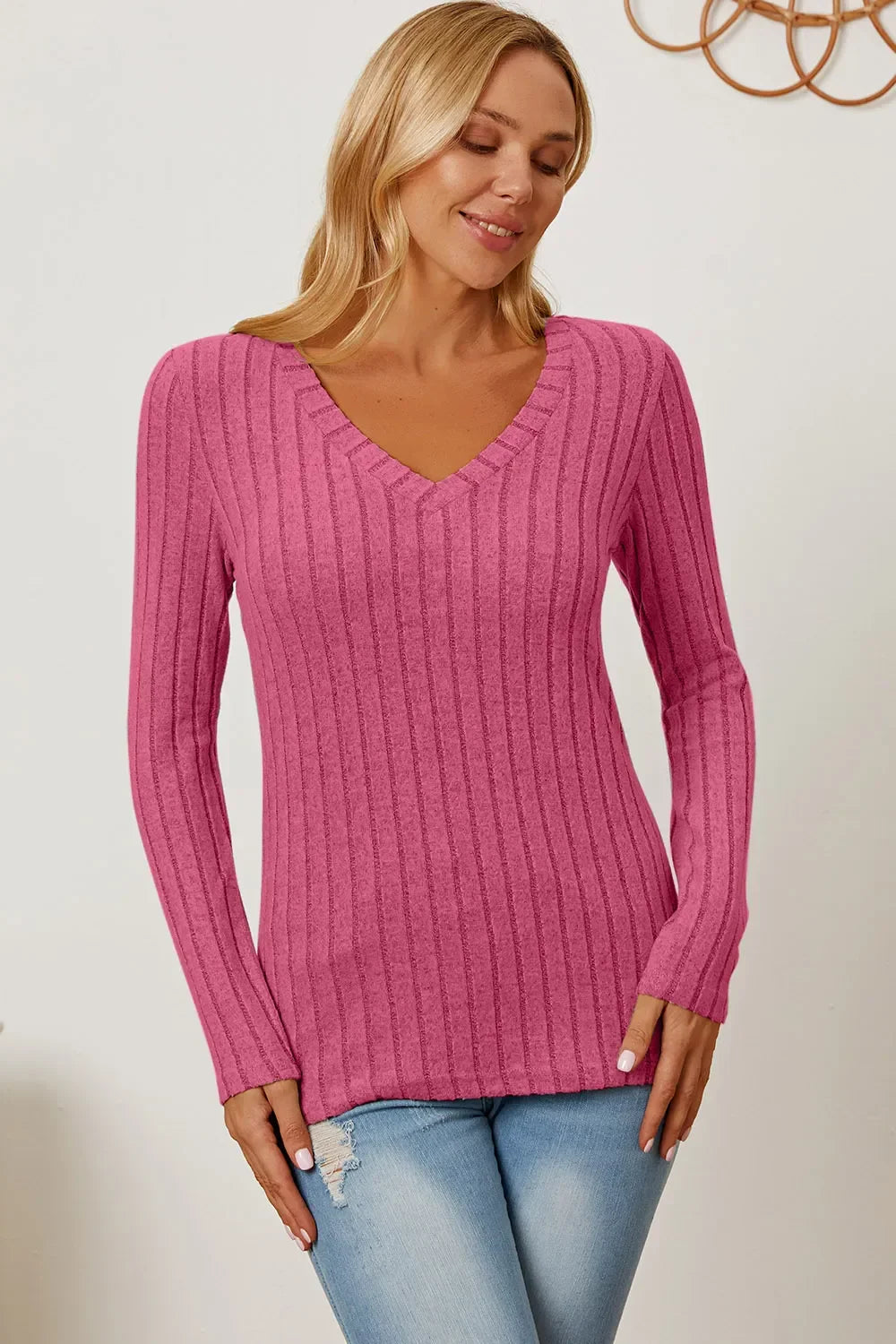 Woman wearing pink ribbed knit V-neck sweater and light blue jeans