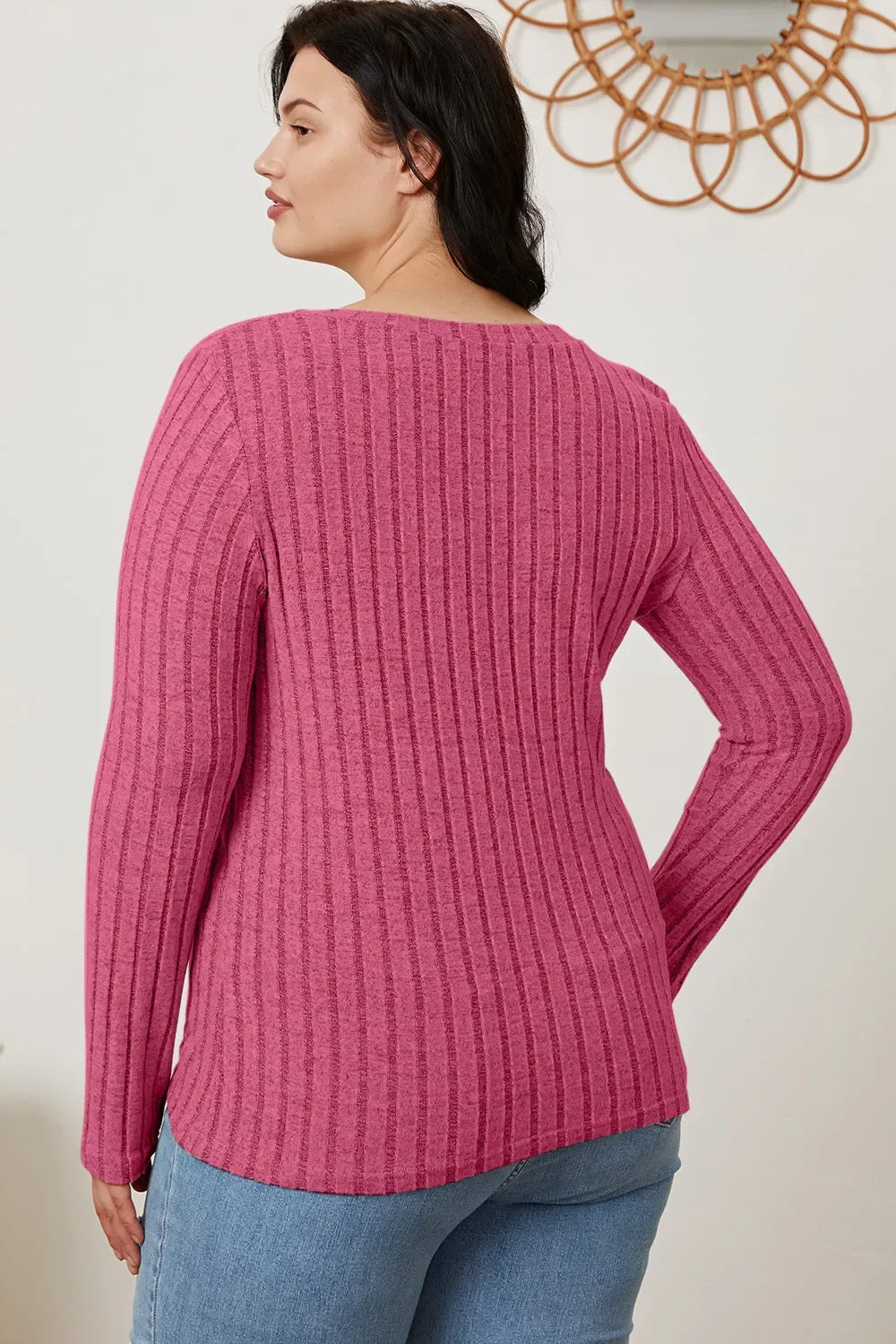 Woman wearing a ribbed pink long sleeve sweater with light wash jeans, back view