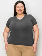 Smiling woman in a fitted dark gray V-neck T-shirt and beige pants on white background