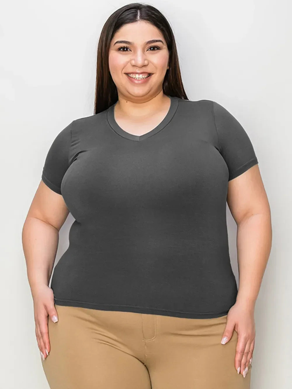 Smiling woman in a fitted dark gray V-neck T-shirt and beige pants on white background