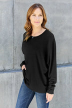 Woman in black long sleeve top and blue jeans standing against a concrete wall