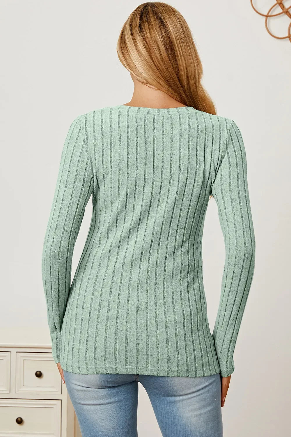 Woman wearing light green ribbed knit sweater and light blue jeans, back view
