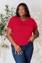 Smiling woman in a bright red short sleeve t-shirt and blue jeans standing by a plant