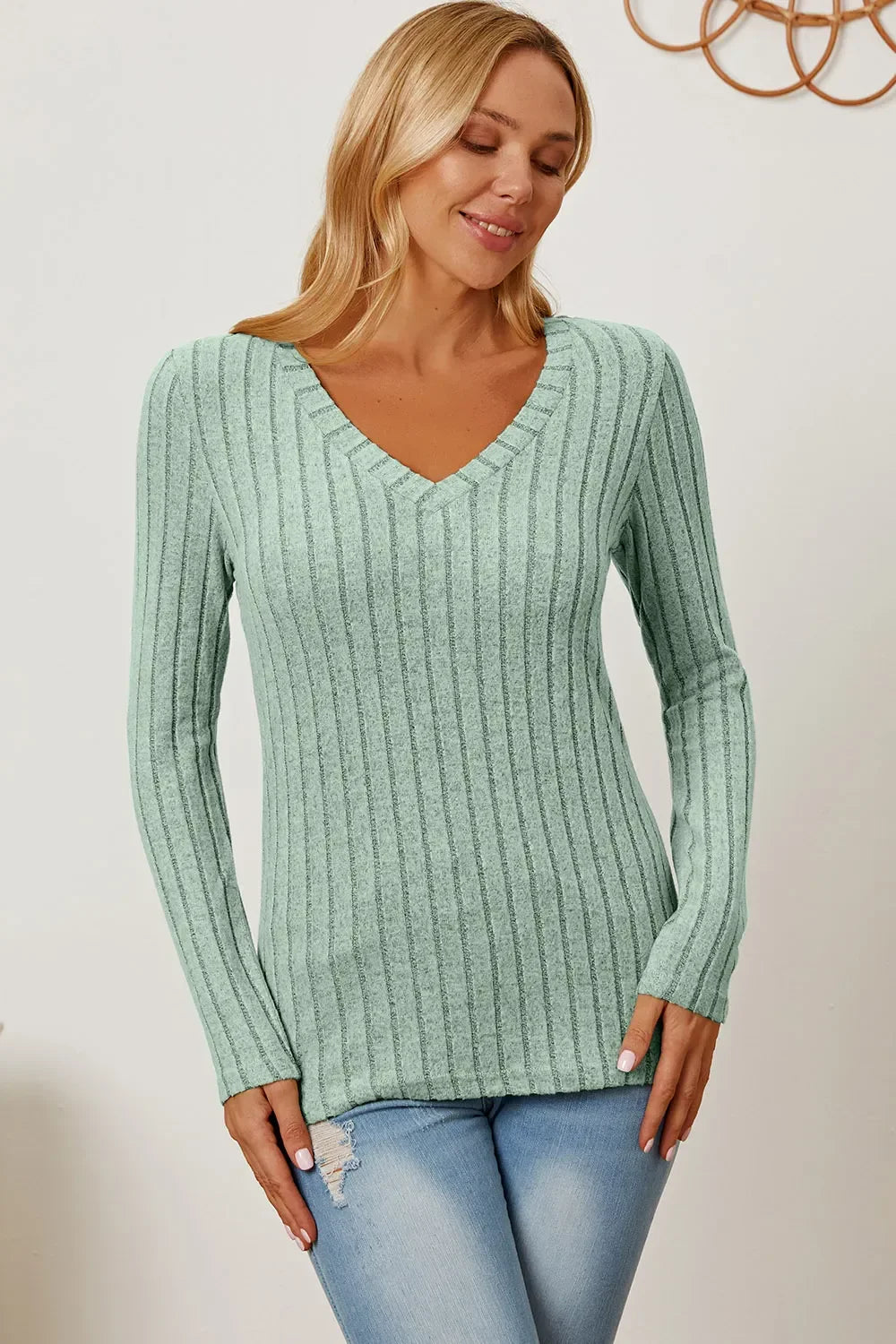 Woman wearing a light green ribbed knit V-neck sweater and light wash jeans