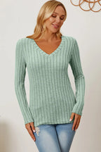 Woman wearing a light green ribbed knit V-neck sweater and light wash jeans