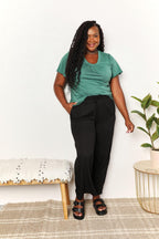Woman in casual green t-shirt, black pants, and sandals standing indoors