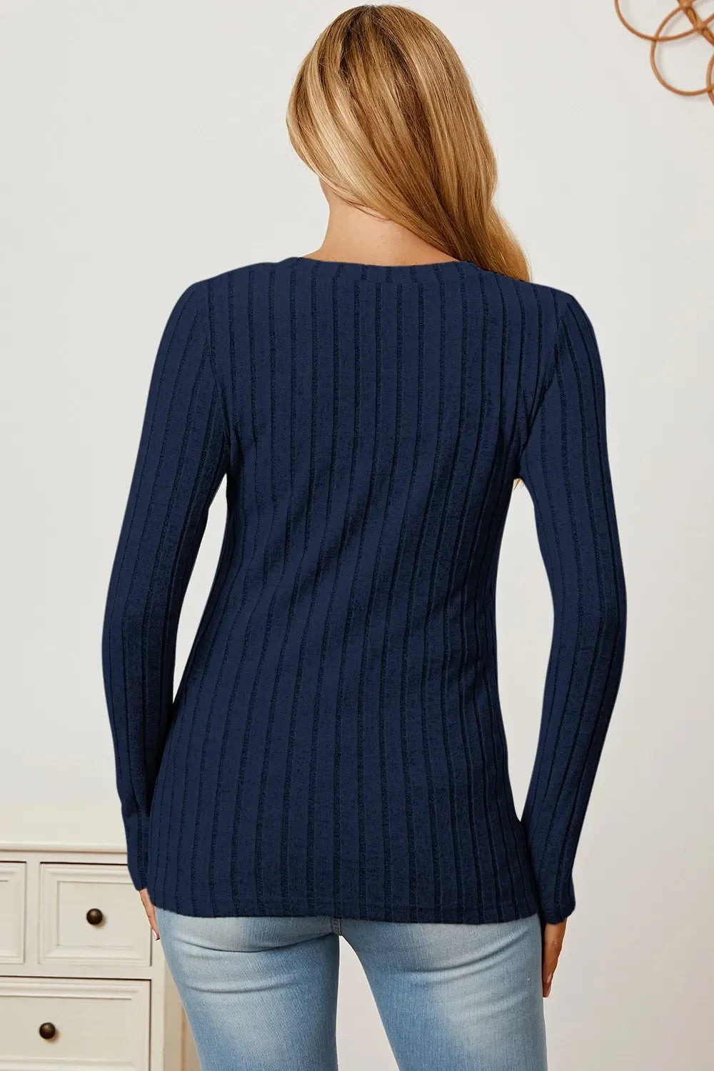 Woman wearing navy blue ribbed long sleeve sweater and light wash jeans, back view