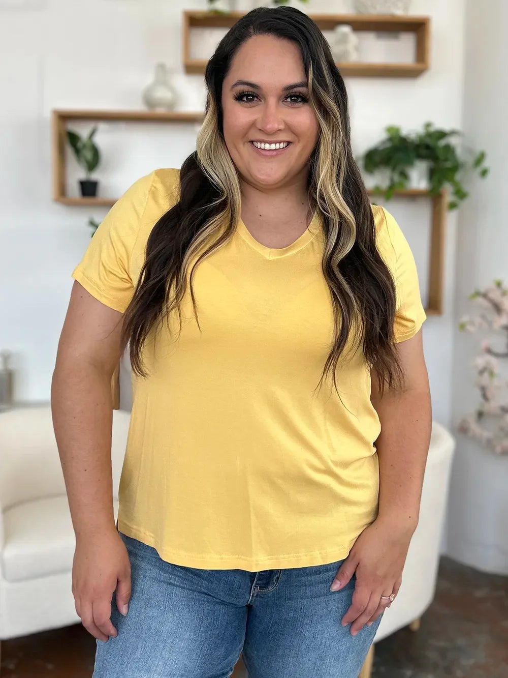 Woman wearing a yellow V-neck T-shirt and blue jeans in a modern living room