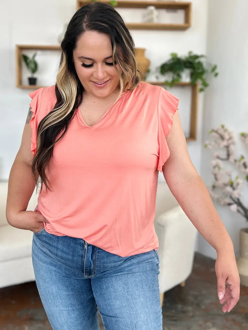 Woman wearing peach flutter sleeve top and blue jeans in modern living room
