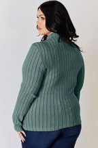 Woman wearing a green ribbed long sleeve sweater and dark blue jeans, seen from behind.